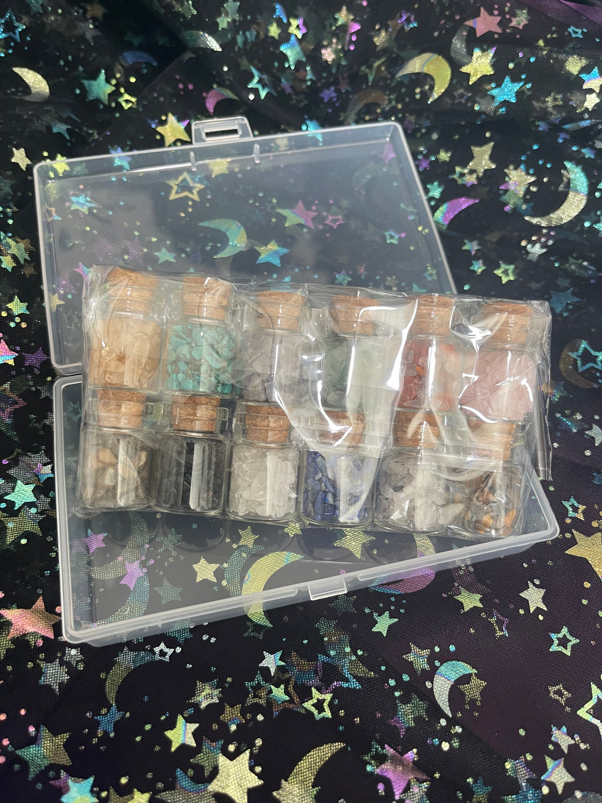 A clear plastic case containing multiple small glass vials with corks, filled with colorful powder or resin pieces, photographed on a black background printed with iridescent stars and crescent moons.